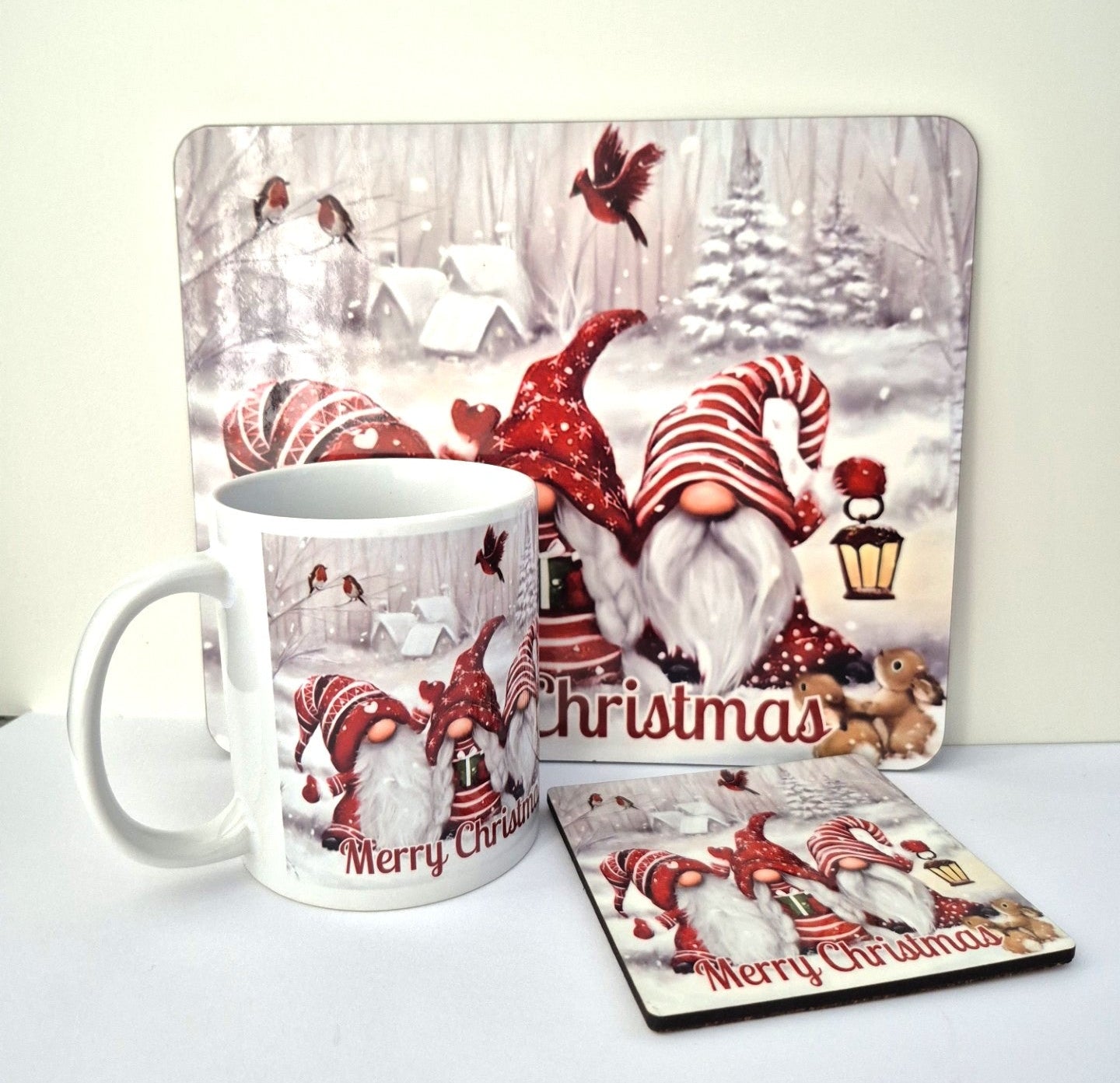 Christmas-themed mug, placemat, and coaster set with gnomes and 'Merry Christmas' text on a white surface.